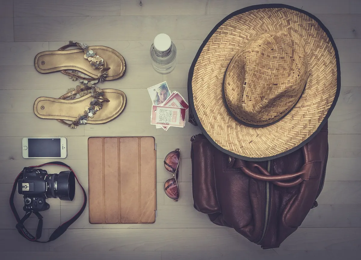 Flat lay of hat, sandals, camera and travel essentials packed with carry-on packing tips