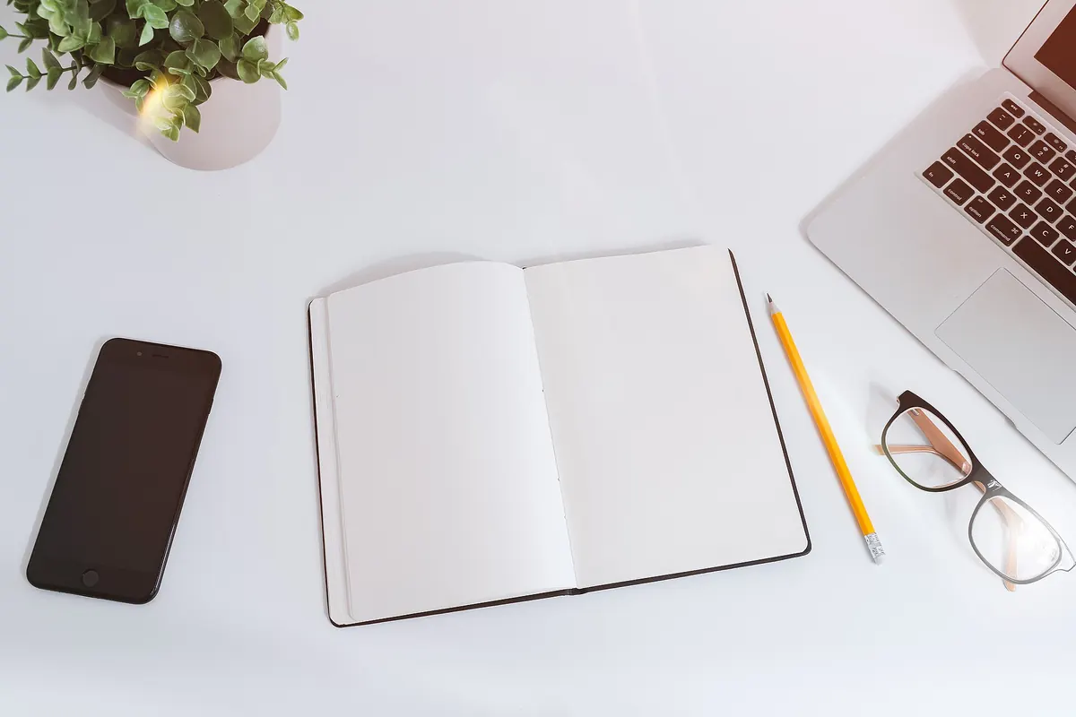 Blank notebook, pencil and laptop on a white desk ready for small business idea validation notes