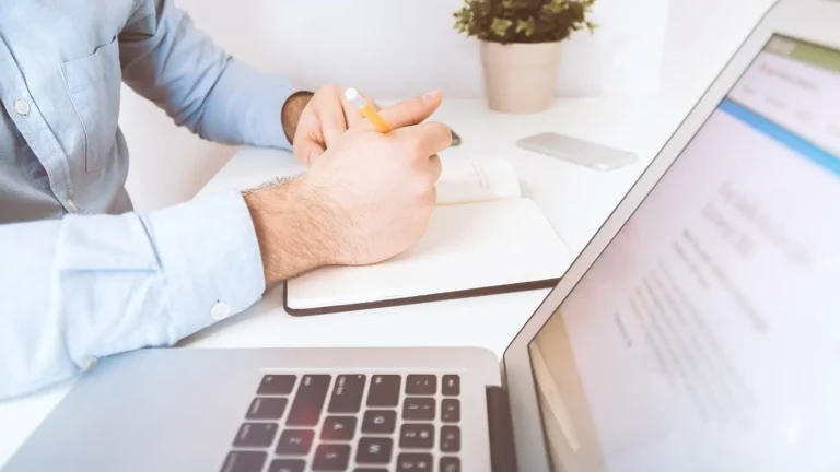 Entrepreneur writing notes beside a laptop while planning how to validate a small business idea
