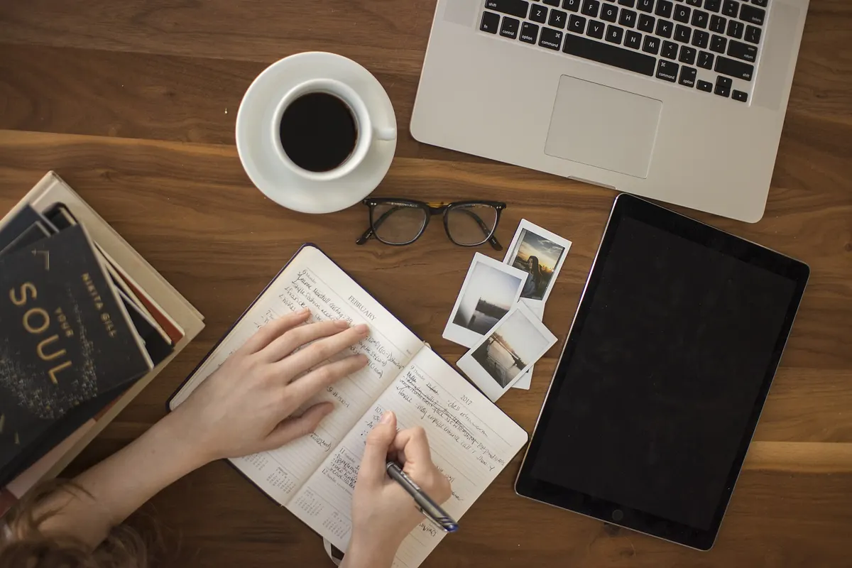 Person journaling beside coffee and a laptop as part of a mindful morning routine