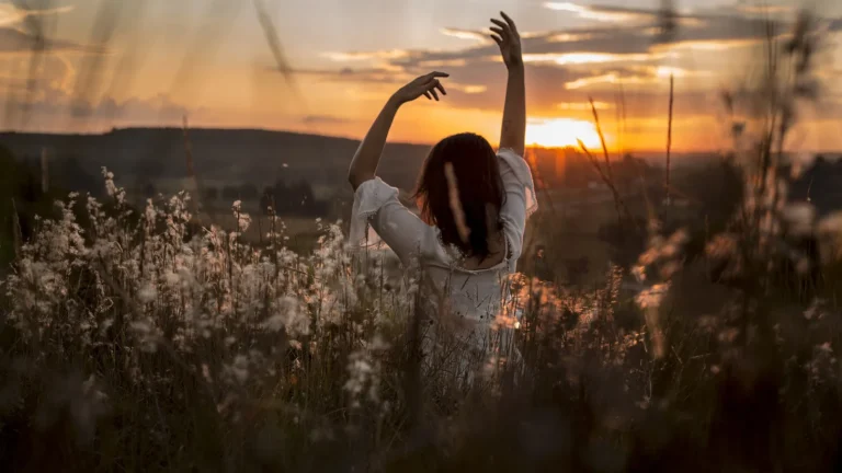 Woman greeting the sunrise in a meadow, representing calm morning routine ideas