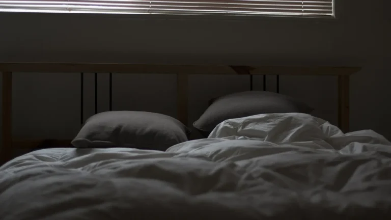 Bed with soft pillows in a dim bedroom, illustrating ways to improve sleep quality naturally