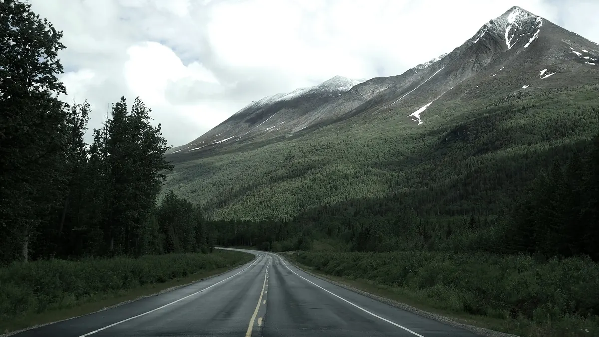 Empty highway winding toward snowy mountains on an affordable road trip