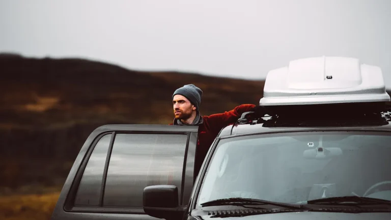 Traveler beside a car with a roof box, ready to plan a budget road trip